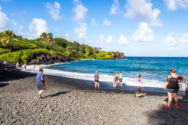 people on edge of black sand beach named Pai’iloa Beach, 