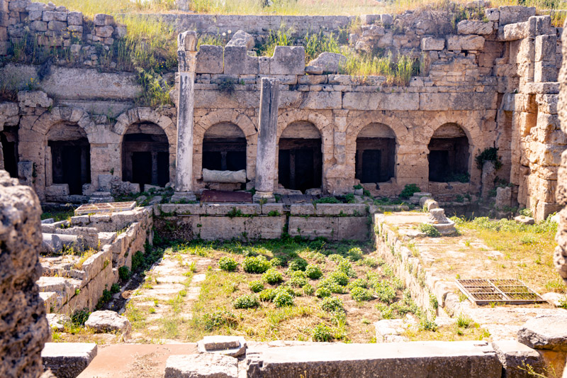 crumbling ruins of Fountain of Peirene around a grassed courtyard