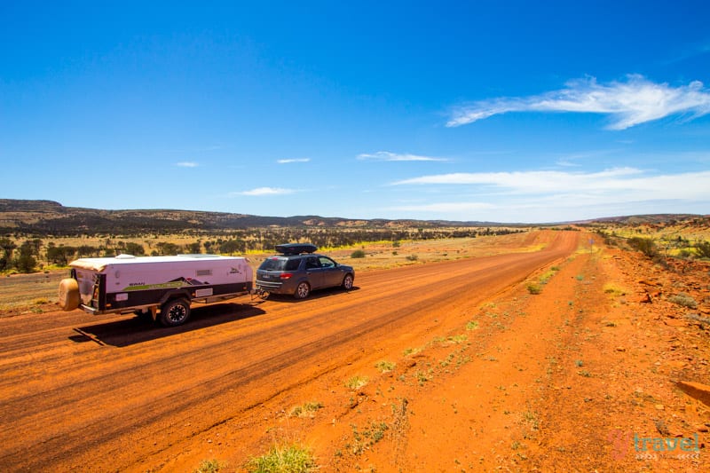 car towing caravan on red dirt road 