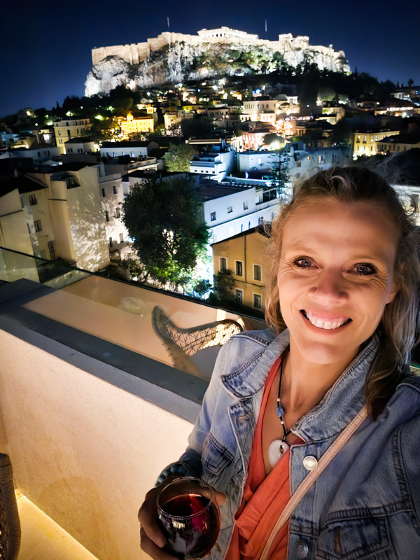 caz taking a selfie with acropolis lit up at night behind her