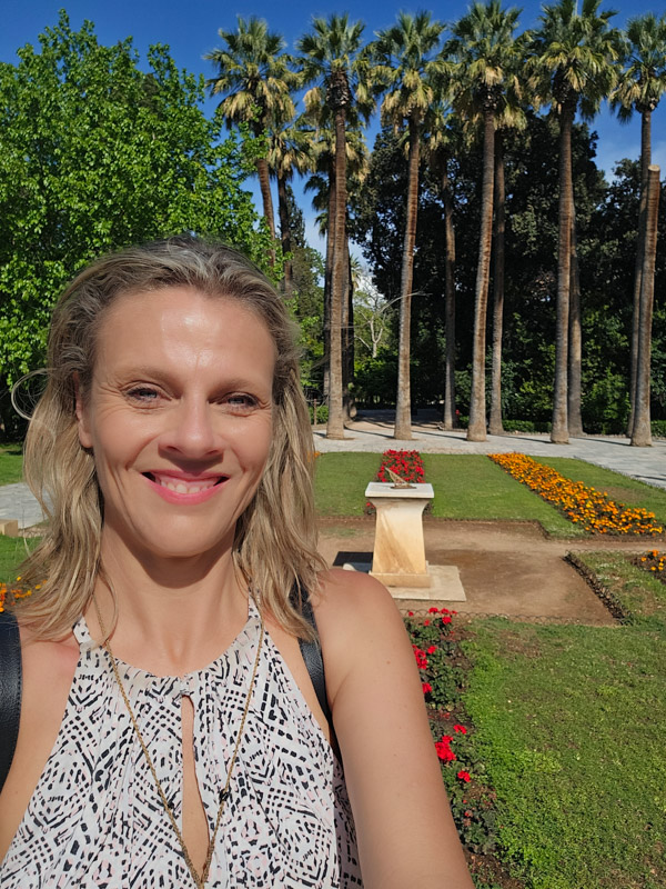 caz taking a selfie in front of a row of palm trees