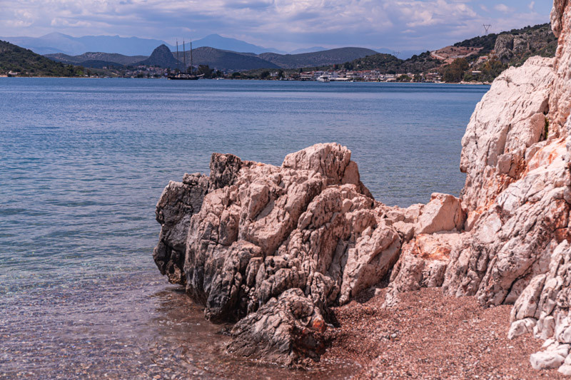 rock sticking out of cliff into water with views of mountains in background