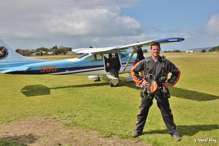 craig in sky diving gear standing beside small plane in field