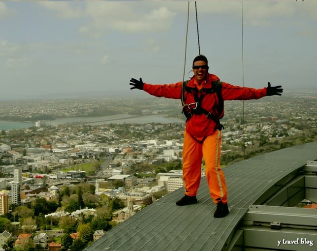 craig standing on edge of narrow platform with arms outstretched and auckland views behind him 