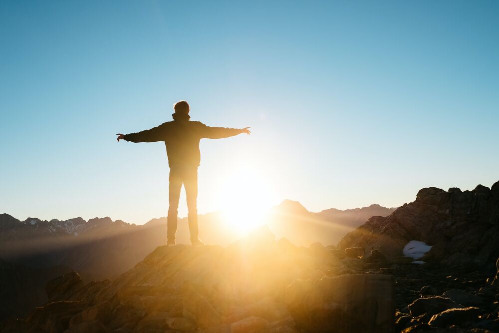 man standing on fliff with arms open