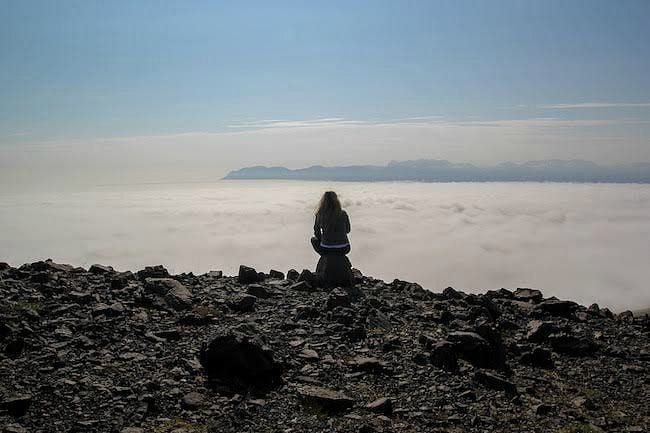 woman sitting on lava rock in Iceland looking at view