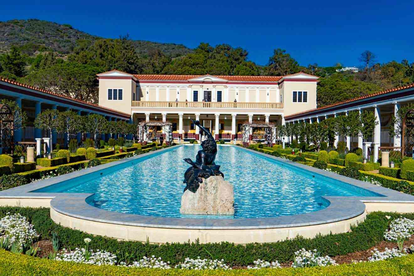 a large white building with a pool in front of it surrounded by lots of greenery