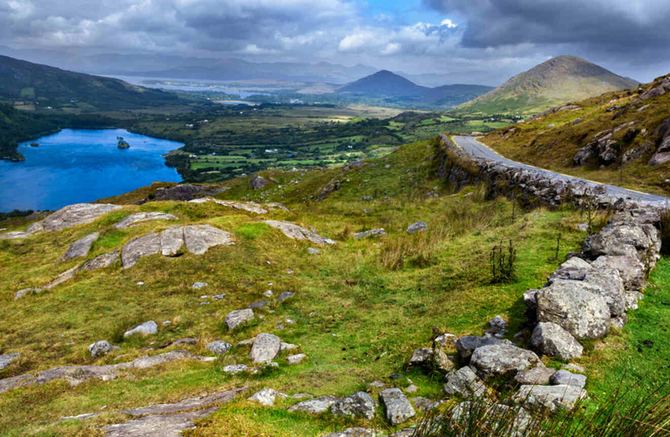 a stone wall on a grassy hill with a lake in the distance