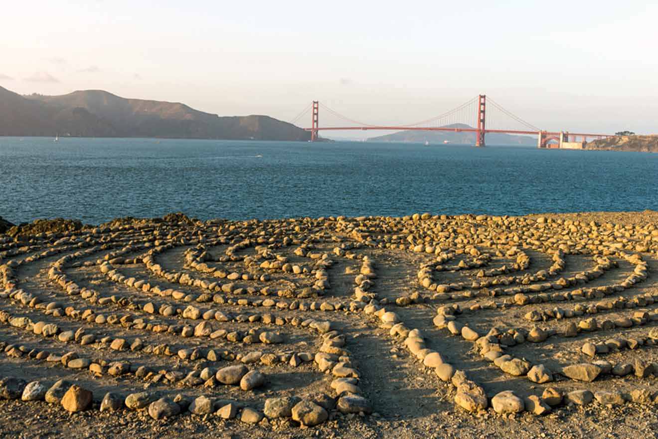 a stone maze in the sand with a bridge in the background