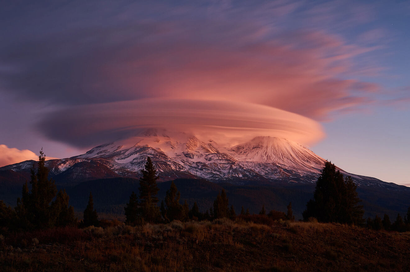 View of snowy mountains covered in clouds at sunset