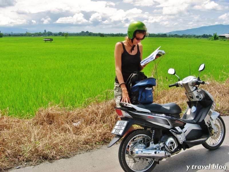 caz standing next to motorbike with helmet on reading lonely planet book.