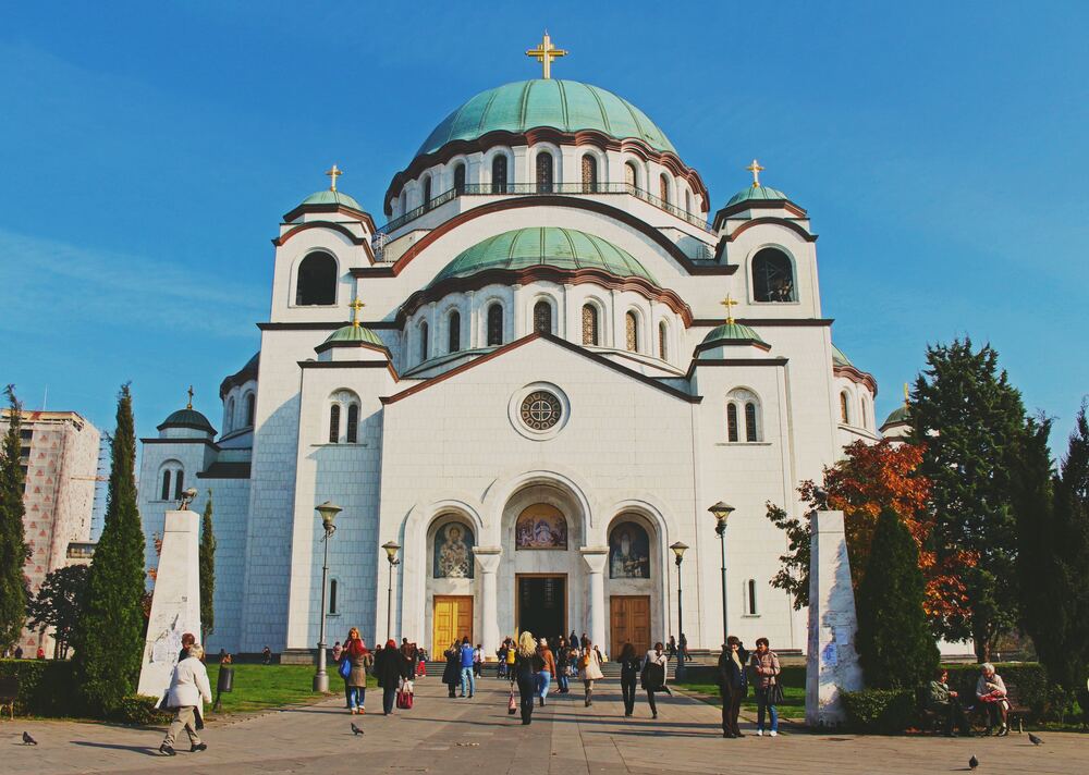 people walking up to the white Temple of St Sava with aqua domed roof