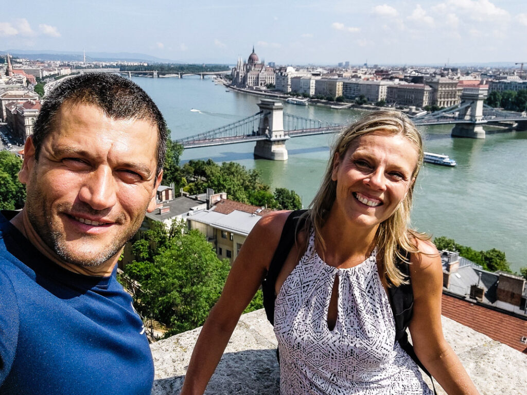 Man and woman hiking with a view of a bridge and river.