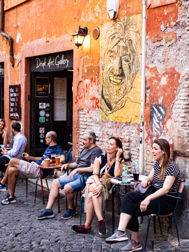 people sitting at tables outside bar on cobblestone street