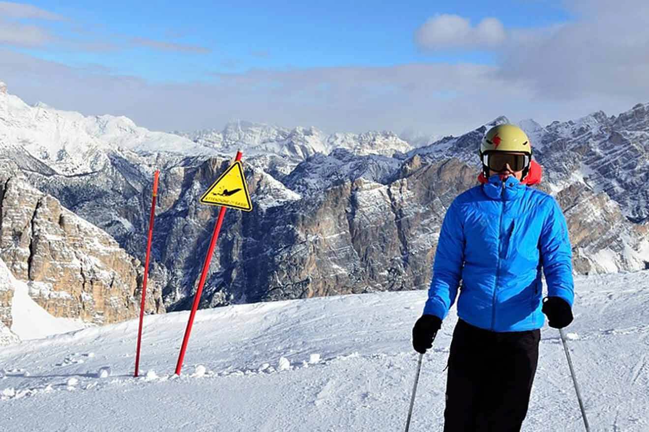 A man in a blue jacket standing on top of a snowy mountain.