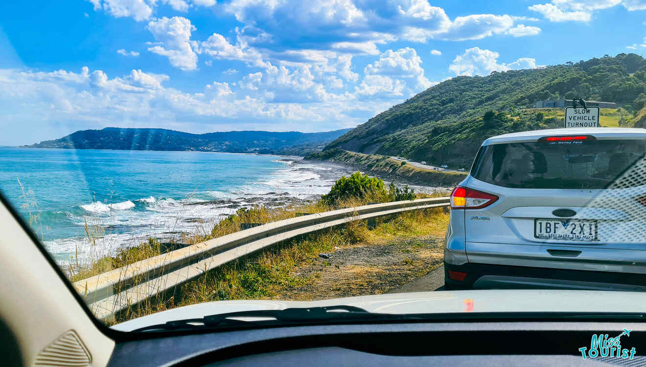 A white car driving down a road next to the ocean.