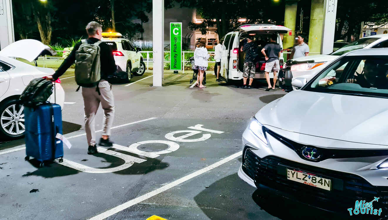 A man is standing next to a parked car with his luggage.