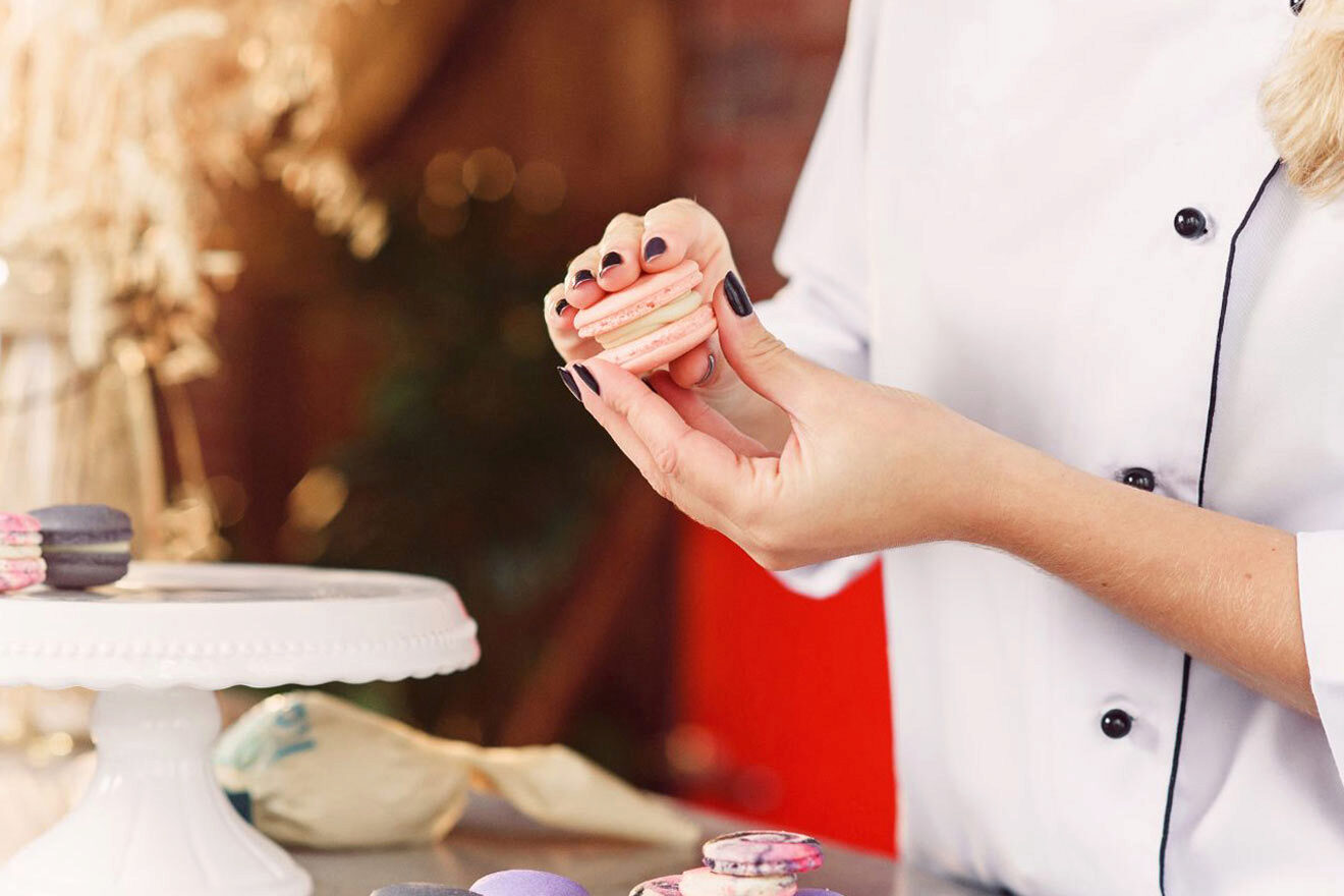 A woman is holding macarons in front of a cake stand