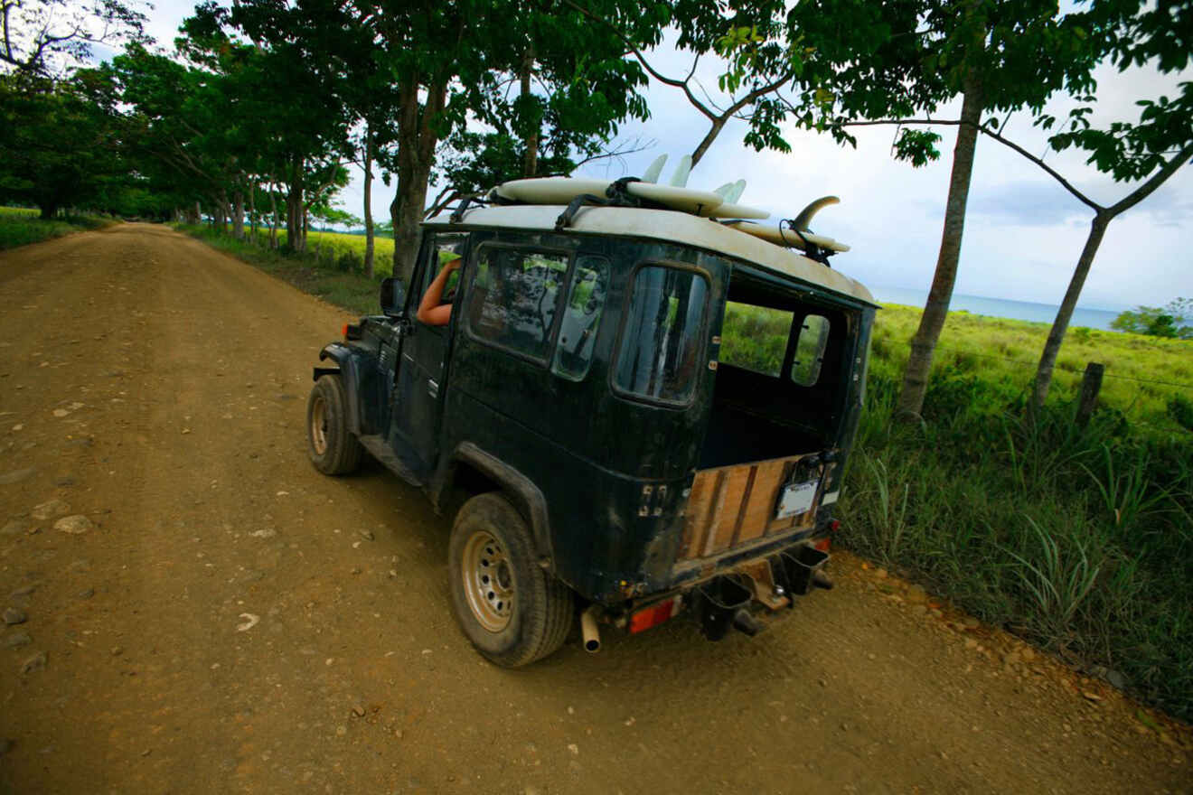 A jeep driving down a dirt road with a surfboard on it.