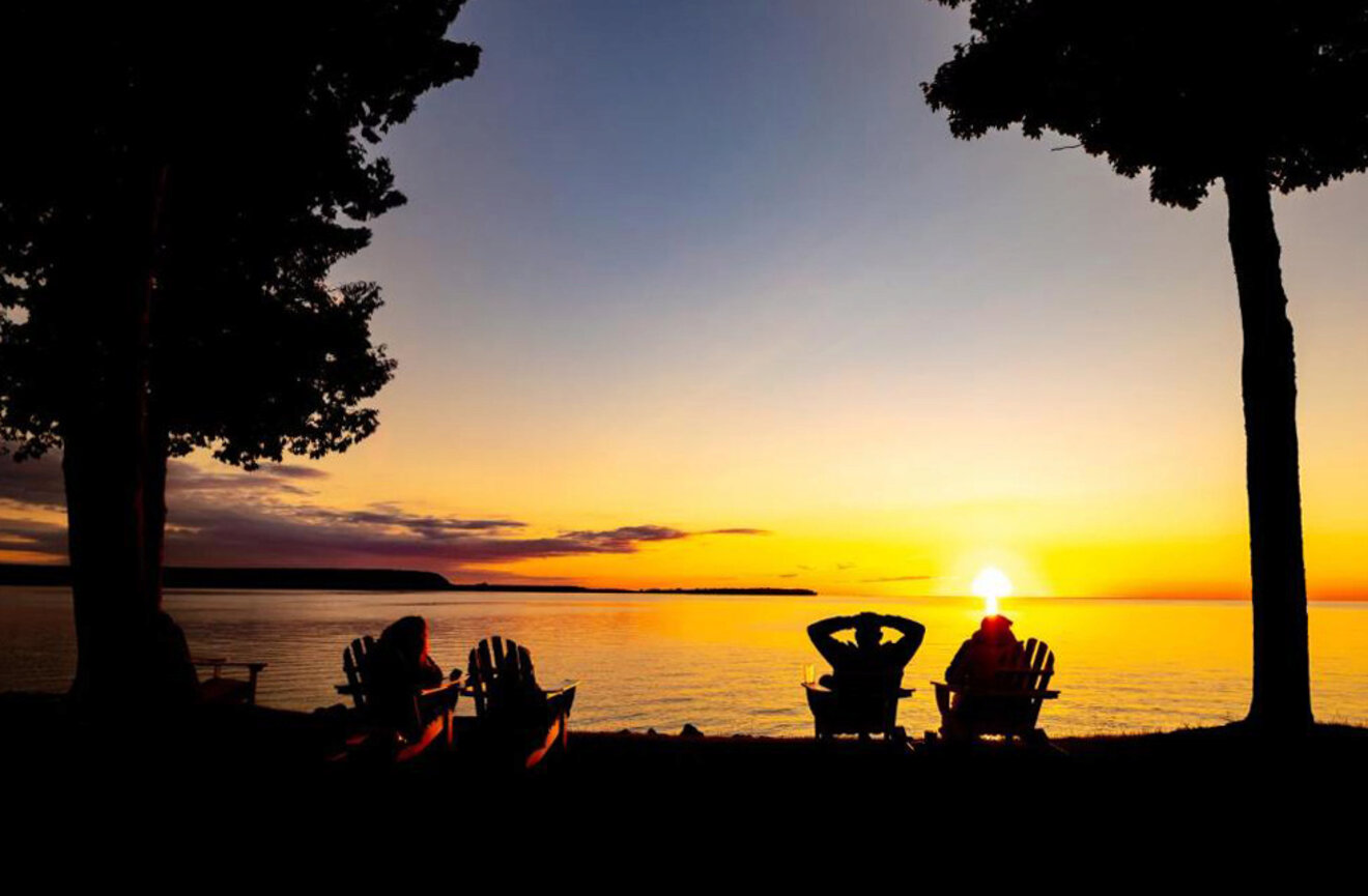 people sitting on lounge chairs looking at the water at sunset