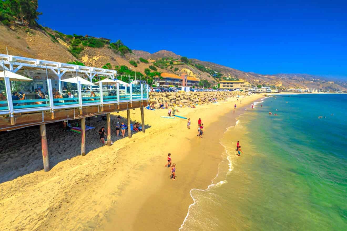 people on the beach next to an oceanfront restaurant