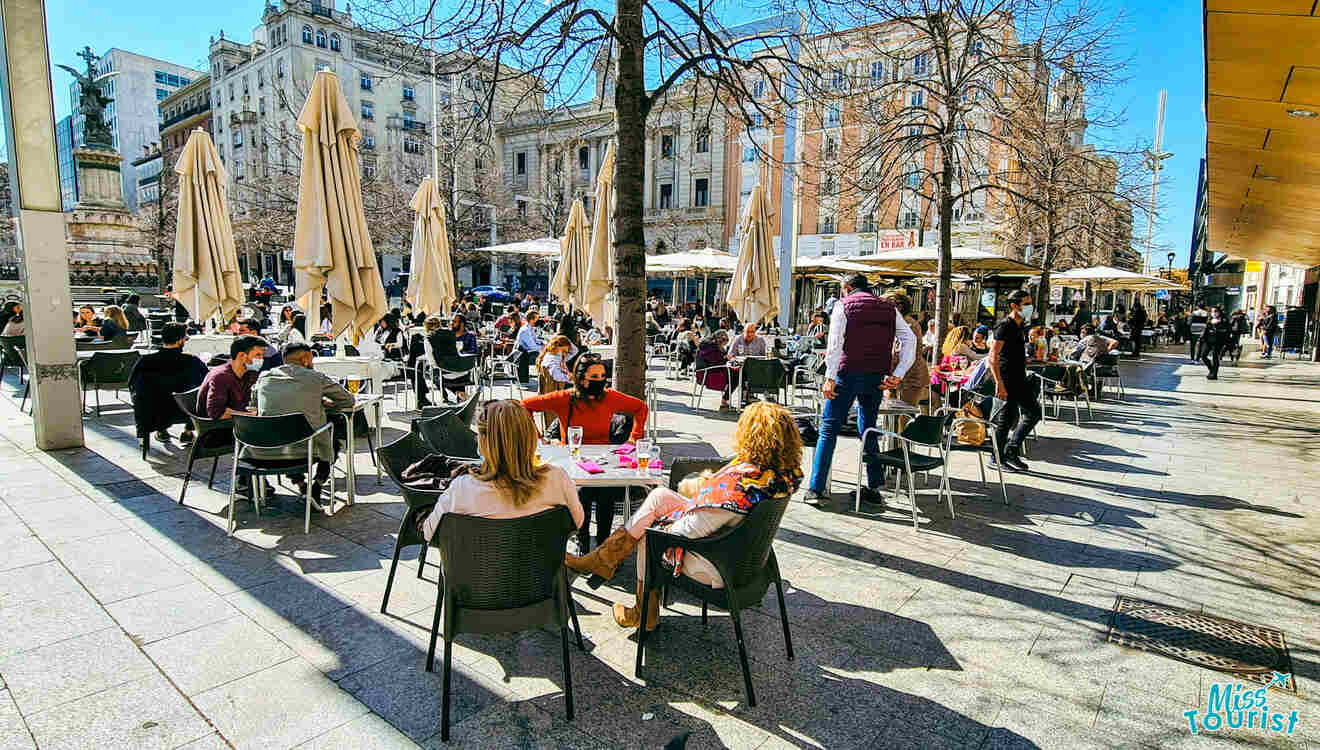 A group of people enjoying drinks and food at tables in a lively city square