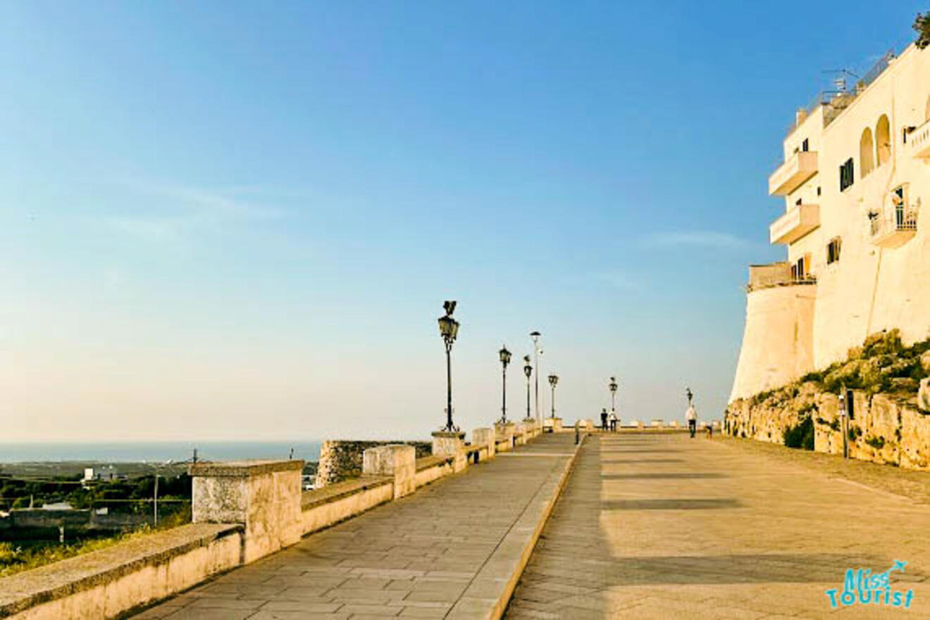 a long walkway next to the ocean with a building in the background