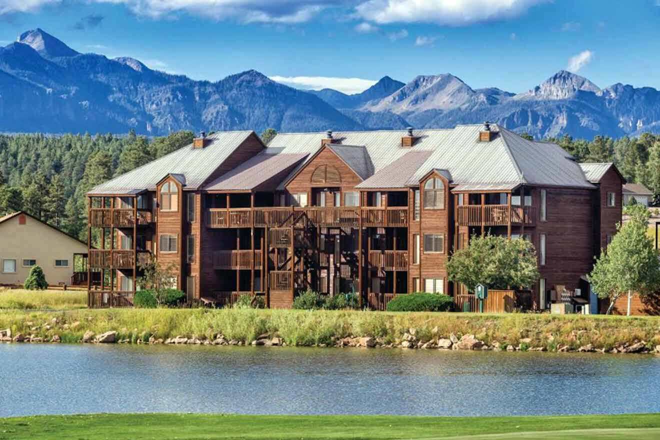 a hotel's building behind a lake with mountains in the background