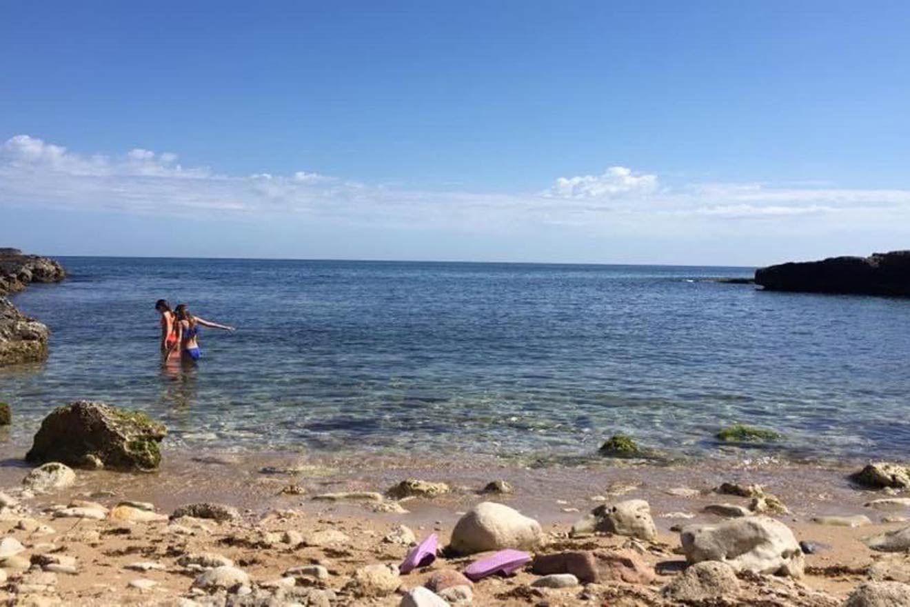 Two people playing in the water near a rocky shore.