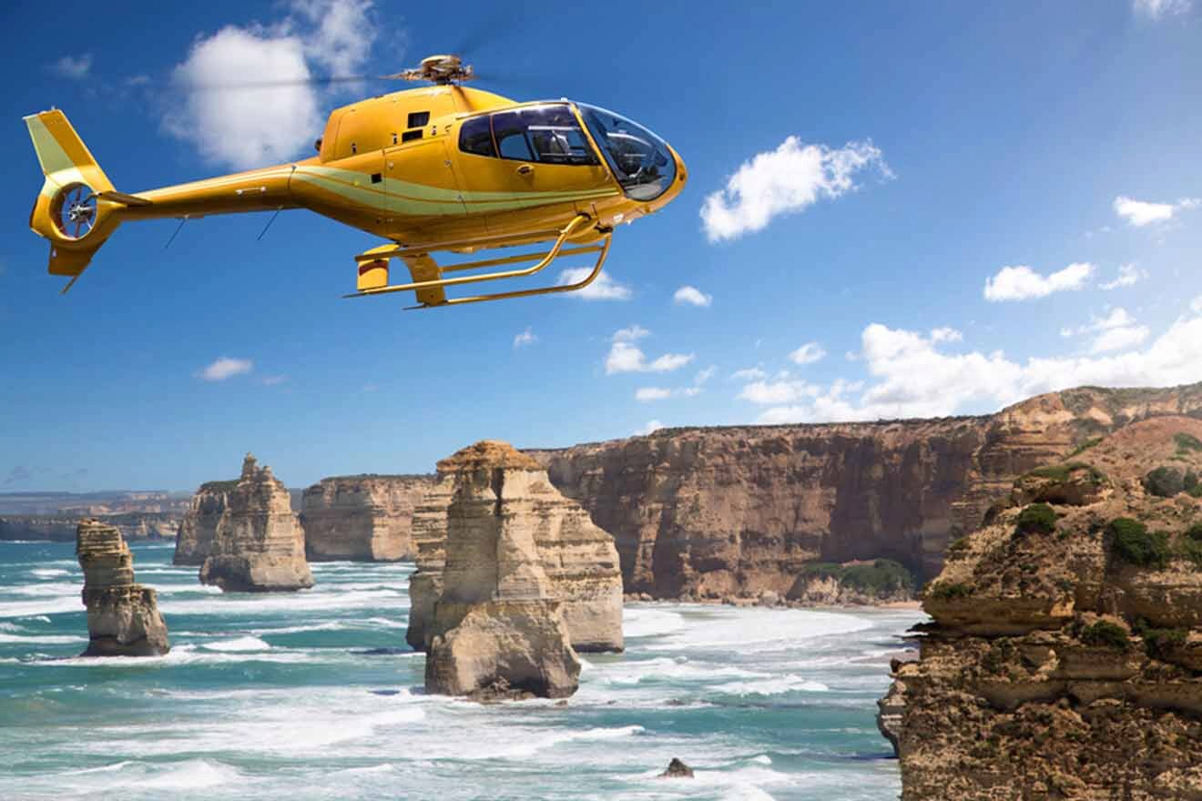 a yellow helicopter flying over the ocean next to rocky cliffs