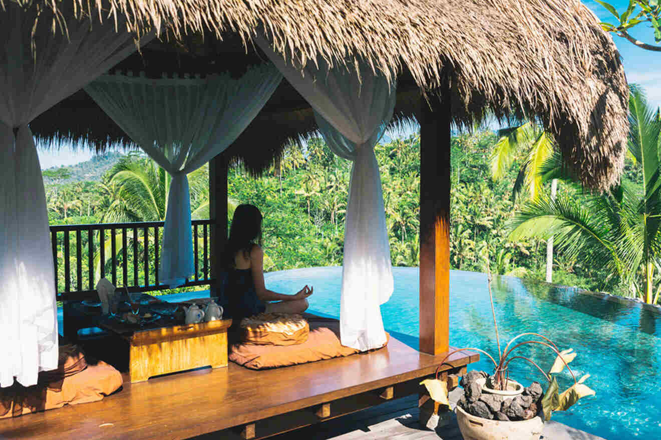 A woman sits on a wooden deck overlooking a pool.