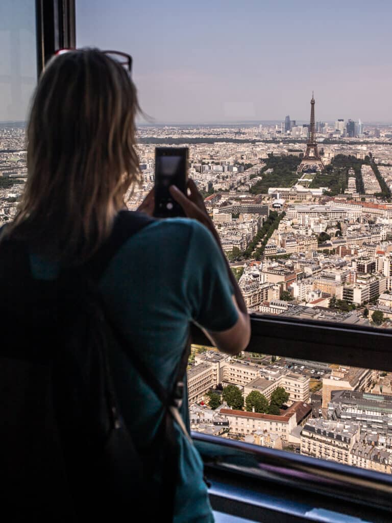 Lady taking photo up high through a window of the Eiffel Tower in Paris