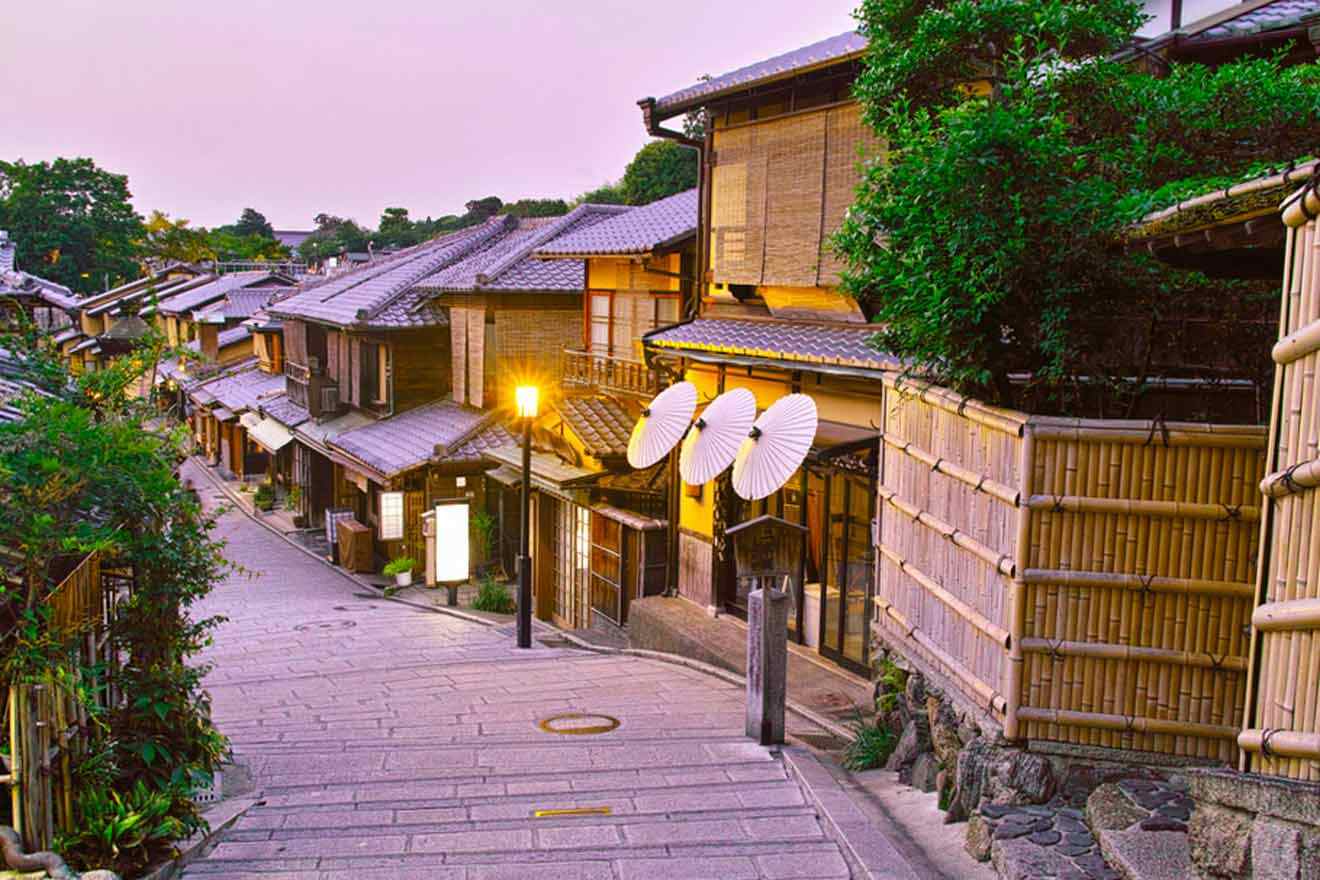 a narrow street lined with wooden Japanese buildings and umbrellas