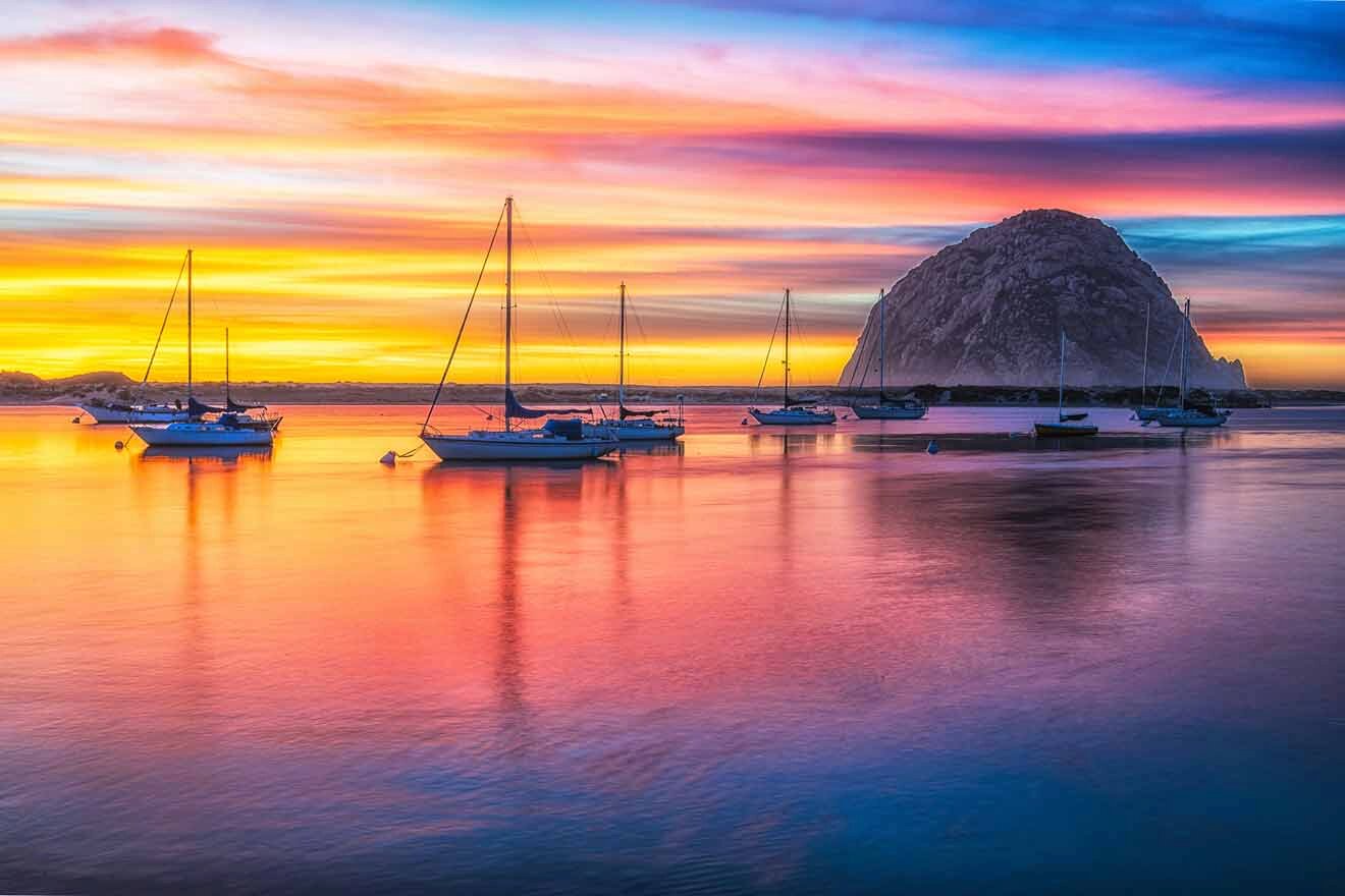 a group of boats floating on top of a body of water with a large rock in the background