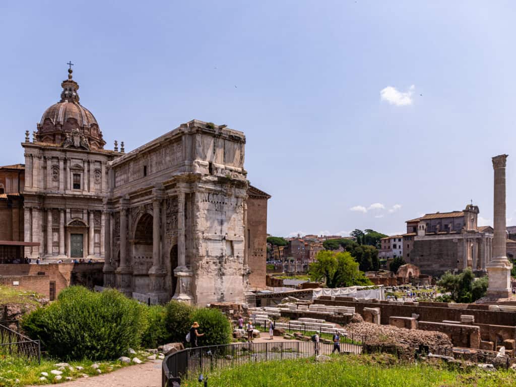 The Arch of Septimius Severus next to domed buildings in the ruins of rome