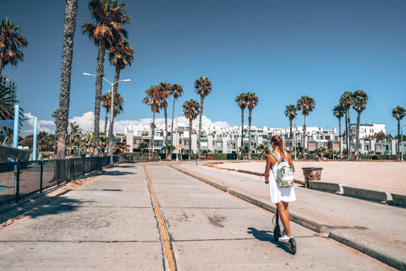 A woman riding a scooter down a sidewalk with palm trees in the background.