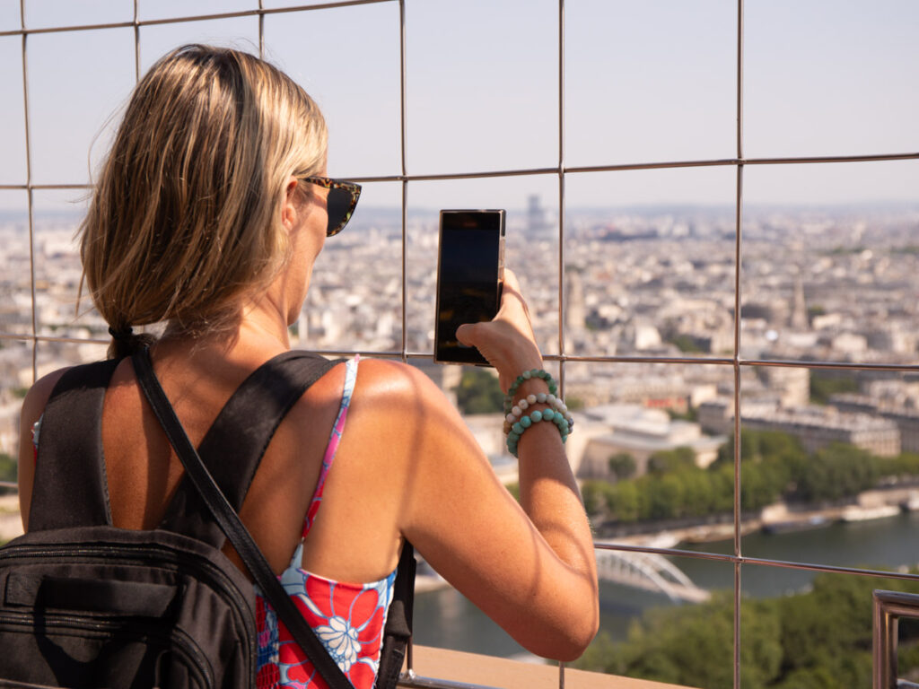 caz taking photo on phone of paris views through chain link fence