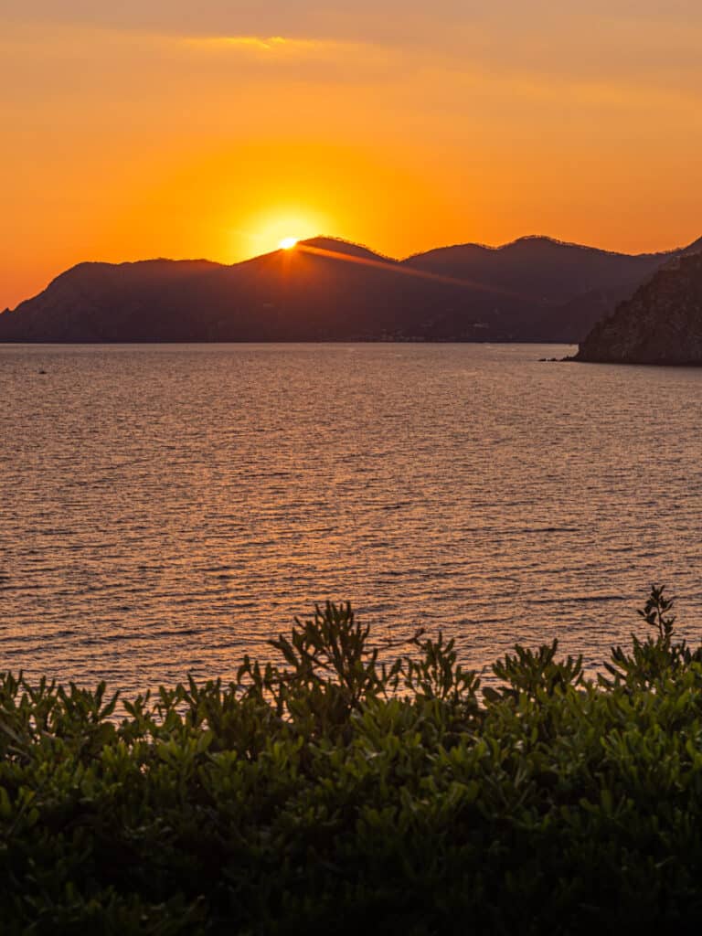 orange sun setting behind the mountain at manarola