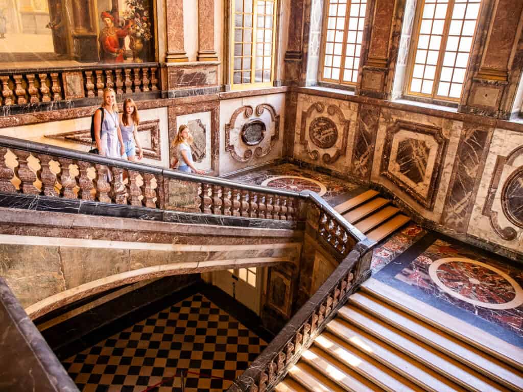 caz and girls walking down elaborate staircase in versailles chateaux.