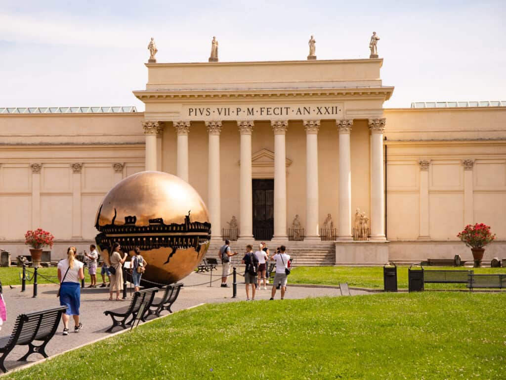 white building with bronze circular sculpture in front of it