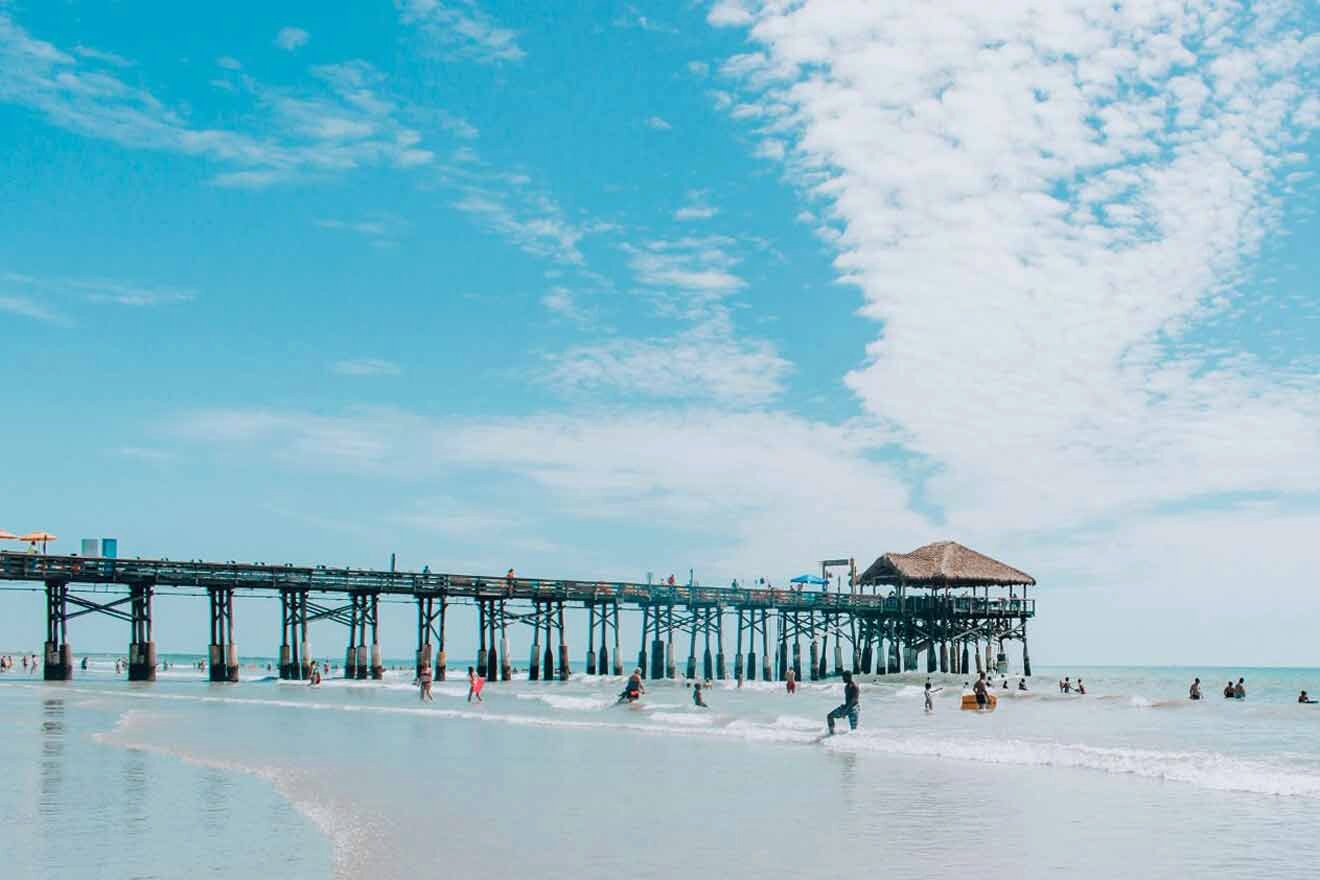 A group of people on the beach near a pier.