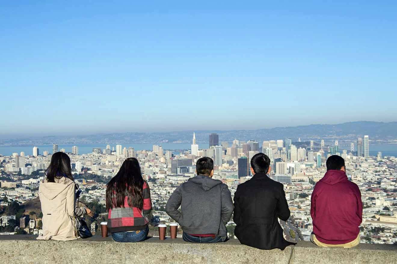 A group of people sitting on a ledge overlooking the city of san francisco.