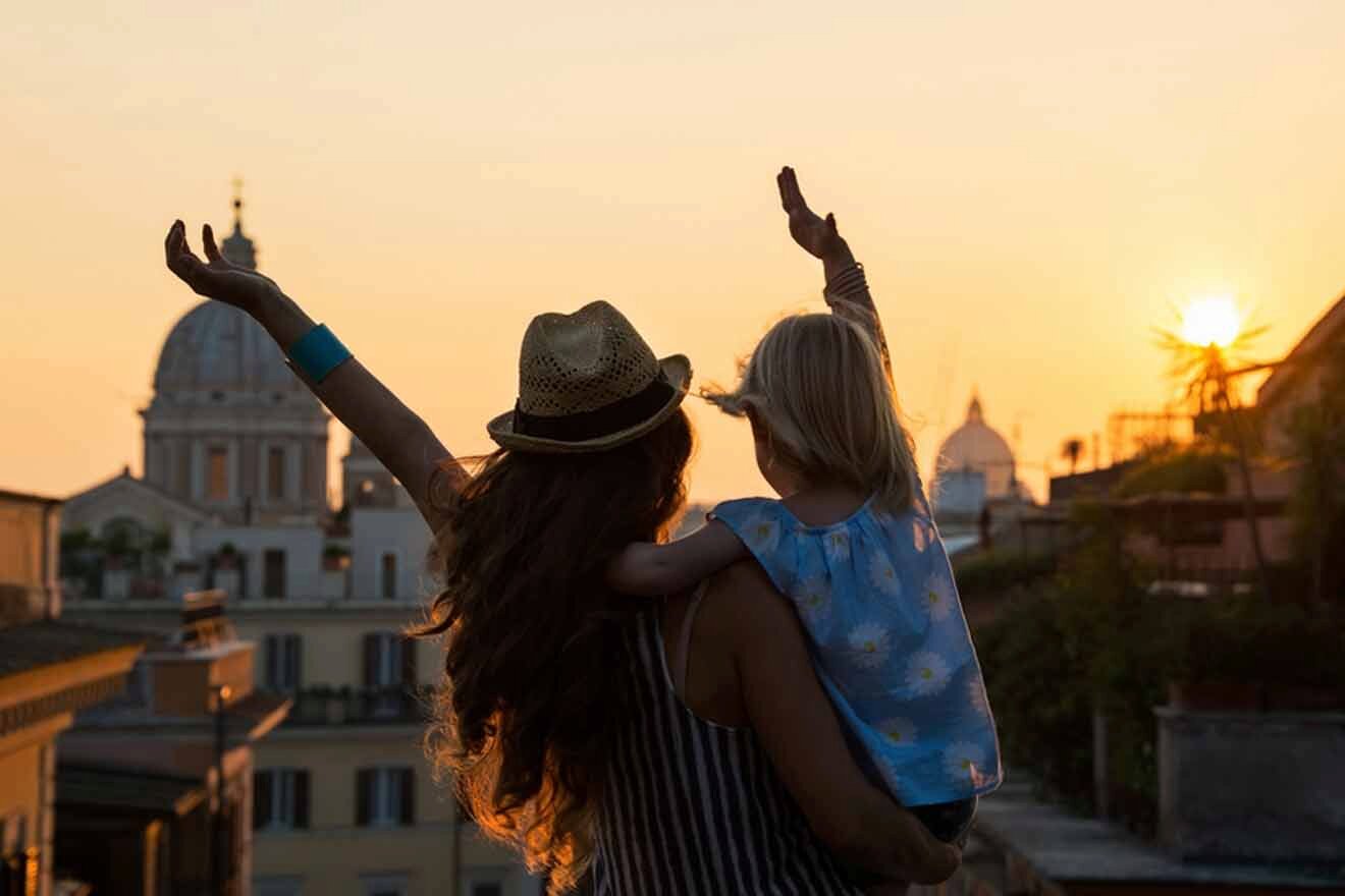 A woman and child with their hands up in the air at sunset in rome.