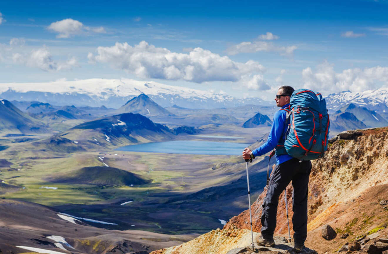 A man with a backpack standing on top of a mountain overlooking a lake.