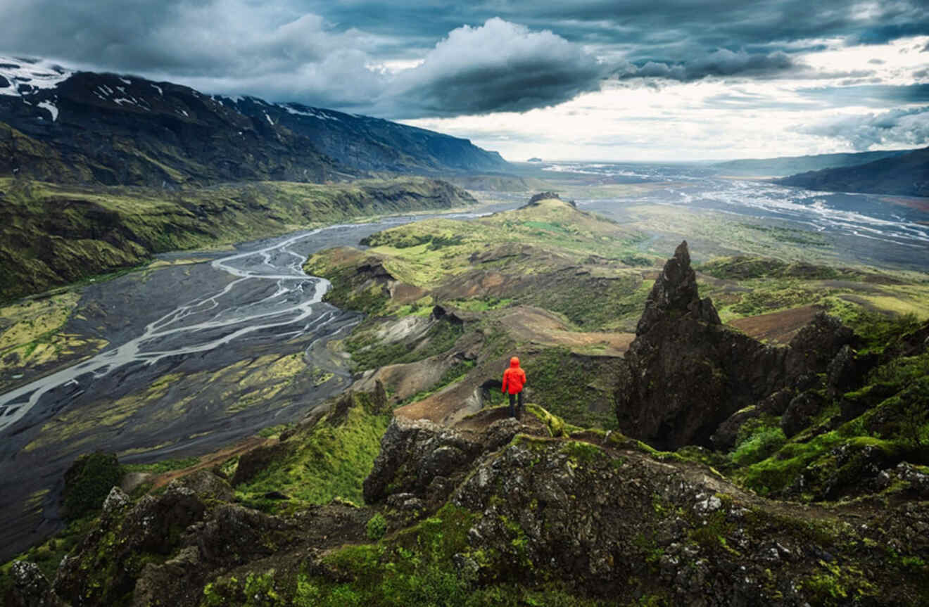 an aerial view of a person standing on top of a mountain peak overlooking mountains and rivers