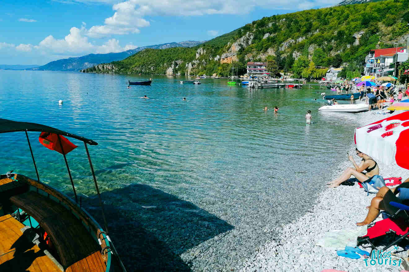 people on a beach with pebbles and crystal clear water