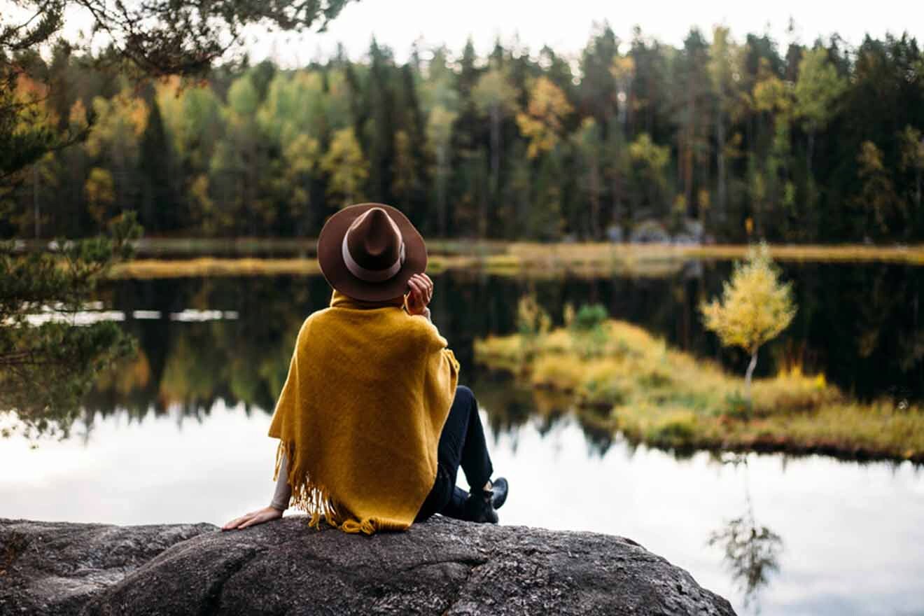 A woman in a yellow hat sitting on a rock overlooking a lake.