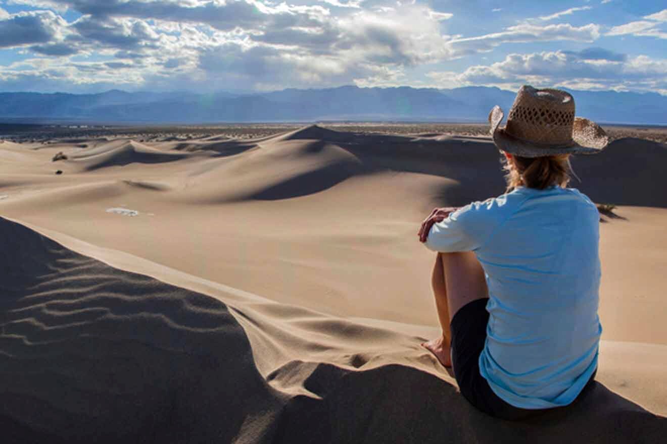 A woman sits on top of a sand dune looking at the sky.