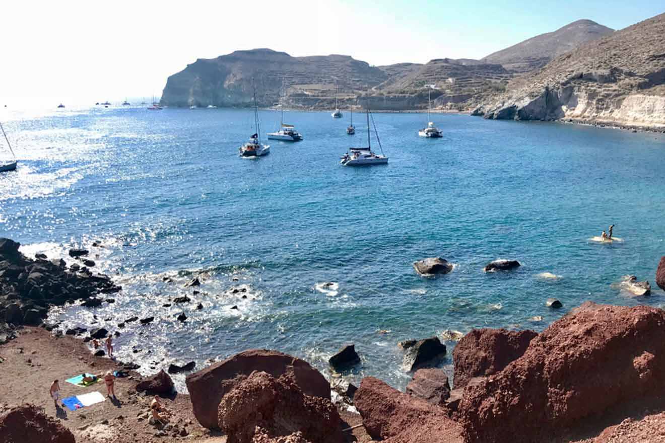 boats in the ocean next to a beach surrounded by hills and rocks