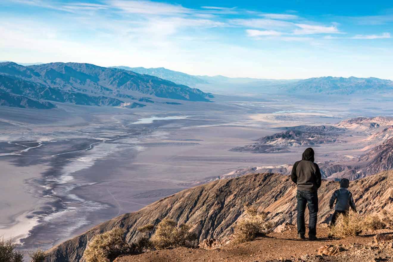 A man and a child standing on a mountain overlooking a valley.